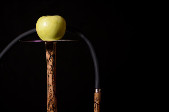Beige wooden hookah with yellow apple on metal plate. Hookah elements on a dark background. Silhouettes of lightning on the stem and mouthpiece.