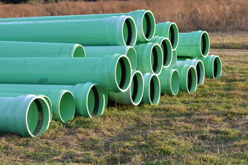 Large pile of empty water main pipes laying in a grassy background in the sunset.