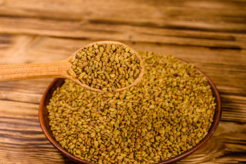 Ceramic plate and spoon with fenugreek seeds on wooden table