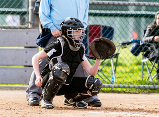 Female softball catcher in full protective gear ready to catch the first pitch.