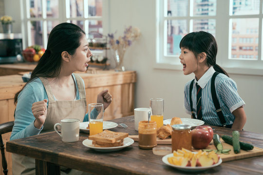 Beautiful asian woman housewife with bad little girl daughter screaming at each other. Concept of family conflict. angry mom and kid in uniform argue in breakfast time in morning before school.