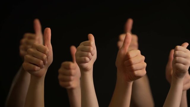 Raising hands with thumbs up on black background.