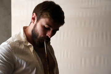 Portrait of a brutal bearded man with short brown hair in a white creased shirt on a white blurred background. Handsome male smokes a hookah and inhales smoke through a wooden mouthpiece.