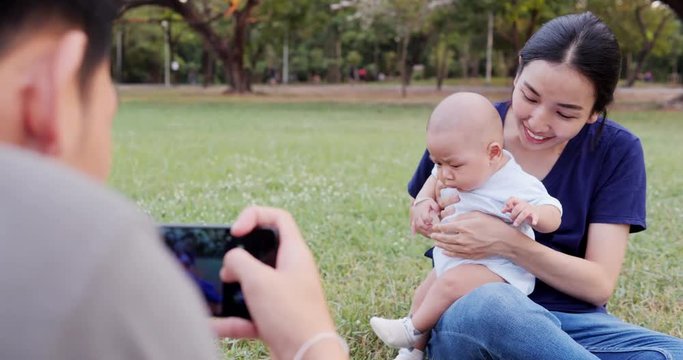 Father using smartphone to taking photo with his wife and baby at park.