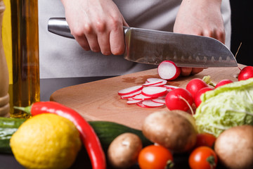 young woman in a gray apron cuts a radish