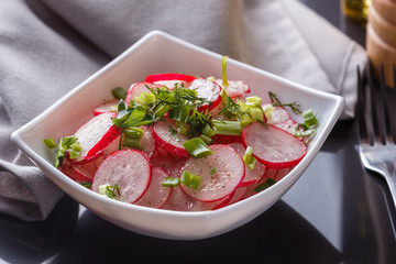 Radish salad in a white bowl on a dark background