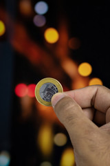 Holding a Brazilian money coin at a blurry background