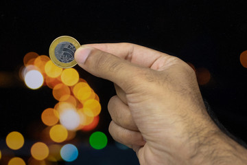 Holding a Brazilian money coin at a blurry background