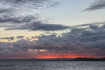 Looking across the water at sunset with dark storm clouds lit up from underneath by a blood red sun...