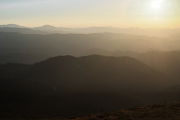Fototapeta premium Góry w słoneczny dzień i zachód słońca z chmurami i lasem iglastym. Krajobraz