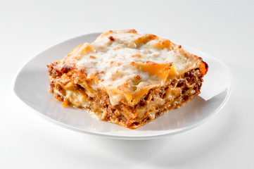 freshly baked lasagna piece on white plate close-up  - obrazy, fototapety, plakaty