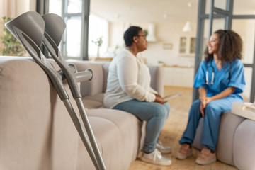 The pair of crutches standing near sofa with patient and nurse
