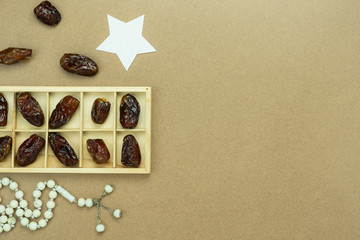 Table top view aerial image of decoration Ramadan Kareem holiday background.Flat lay date with rosary & star paper.Essential object on modern rustic brown wooden at office desk.copy space