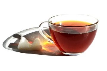 Hot black tea in transparent glass cup with long rainbow shadow in shaft of sunlight and two pieces of sugar in shape of heart on White background. Isolated