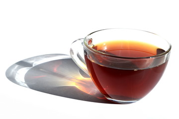 Hot black tea in transparent glass cup with long rainbow shadow in rays of sunlight on White...