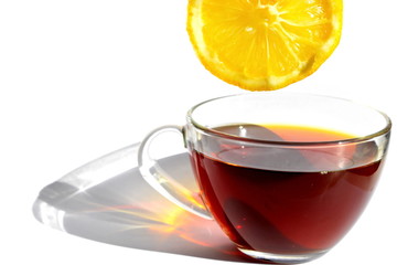 Transparent glass cup of hot black tea with long rainbow shadow in morning rays of sunlight and yellow slice of bitter sour lemon on white background. Isolated