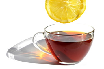 Yellow slice of bitter sour lemon over transparent glass cup of hot black tea with long rainbow...