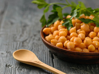 Parsley branch on a bowl with boiled chickpeas on a black table.