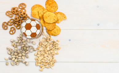 Beer with a soccer ball on a beer foam and snacks on wooden background. Empty space for text