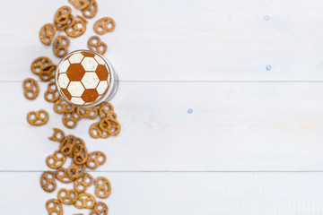 Beer with a soccer ball on a beer foam and pretzels on wooden background. Top view. Empty space for text