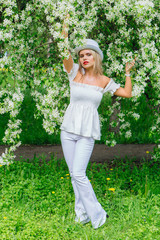 Sexy modern bride in white cylinder hat enjoing blooming apple tree flowers.