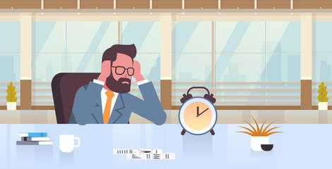 tired businessman holding head by two hands business man sitting workplace desk with alarm clock deadline time management concept modern office interior male cartoon character portrait flat