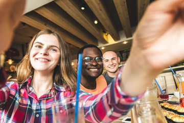 Group of young cheerful friends are sitting in a cafe, eating, drinking drinks. Friends take selfies and take pictures.
