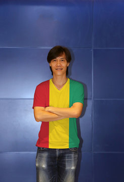 Man wearing Guinea flag pattern shirt and cross one's arm on the blue wall background.
