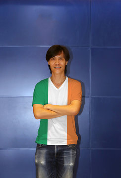 Man wearing Ireland flag pattern shirt and cross one's arm on the blue wall background.