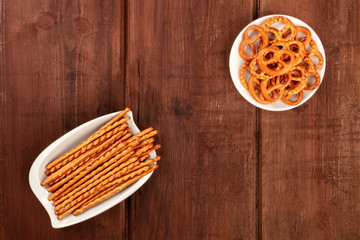 An overhead photo of salty crackers. Sticks and pretzels, shot from above on a dark wooden background with copy space. Party snacks banner with a place for text