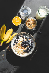 Healthy breakfast granola bowl with banana, blueberry and milk on a black concrete background. Top view. Harsh light food photography