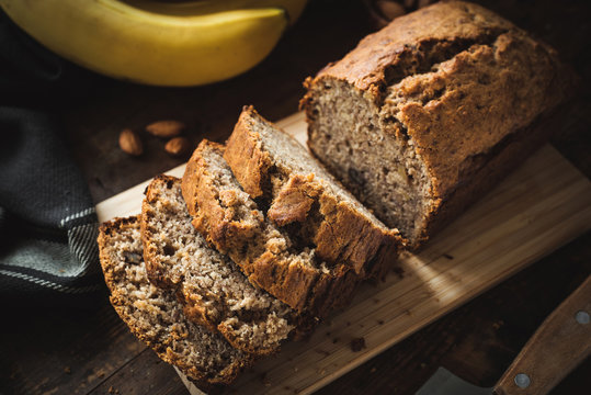 Homemade banana bread or cake loaf sliced on wood. Soft morning light, dark moody food photography. Closeup view