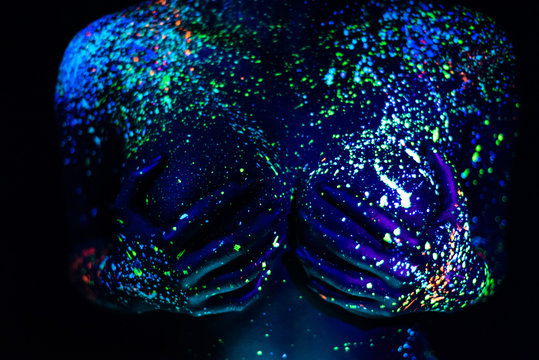 Ultraviolet body art blue night sky with stars. Fluorescent paint on a large female breast covered with hands.