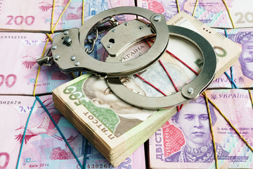 Handcuffs on Ukrainian currency hryvnia. Corruption and financial crime or penalty.