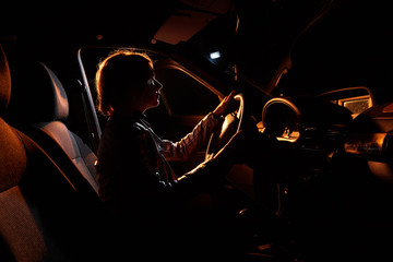 Fashionable young woman in a car in the night and colour light behing her