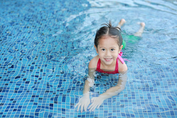 Fototapeta na wymiar Cute little Asian child girl in a mermaid suit has fun sitting poolside.