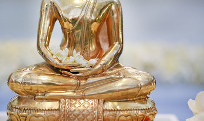 Closeup golden Buddha statue with Jasmine flower on hands.