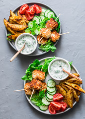 Big lunch plate - fish kebabs, roasted lemon potatoes, tzatziki sauce and fresh vegetables on a gray background, top view