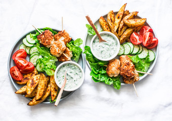 Big lunch plate - fish kebabs, roasted lemon potatoes, tzatziki sauce and fresh vegetables on a light background, top view