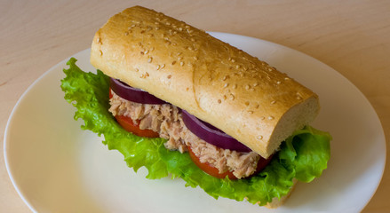 Tuna sandwich on wooden table. White plate. Tuna, lettuce, onion, tomato, bread.