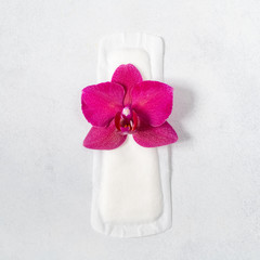 Fototapeta na wymiar Menstrual pad with orchid on light grey background. Concept of critical days, menstruation or woman's health. Top view, flat lay.