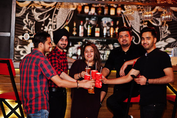  Group of indian friends having fun and rest at night club, drinking cocktails, clinking and cheers near bar counter.