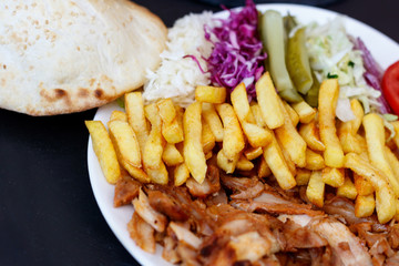 Chiken Doner Kebab on the plate with bread, french fries, tomatoes, onion, pickles and salad on a dark background. Grilled chicken meat with vegetables.