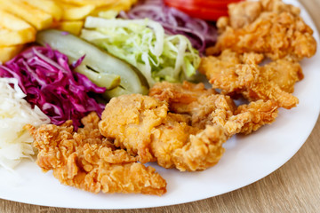 Chicken wings on the plate with french fries, tomatoes, onion, pickles and cabbage salad on a wooden background.