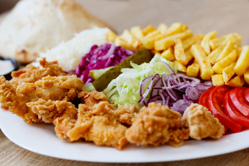 Chicken wings on the plate with bread, sauce, french fries, tomatoes, onion, pickles and cabbage salad on a wooden background.