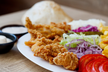 Chicken wings on the plate with bread, sauce, french fries, tomatoes, onion, pickles and cabbage salad on a wooden background.