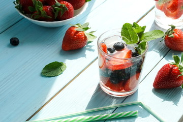 refreshing summer drinks with fresh strawberries and blueberries on grey wooden surface, table, background. copy space