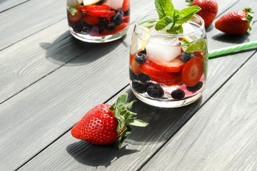 refreshing summer drinks with fresh strawberries and blueberries on grey wooden surface, table, background. copy space