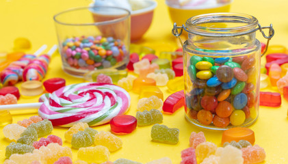 Colorful candies assortment on yellow color background, closeup view