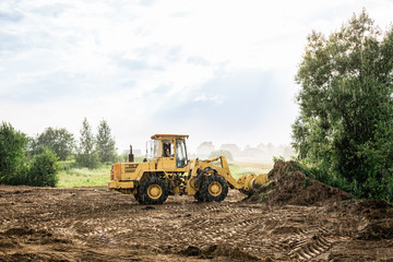 large yellow wheel loader aligns a piece of land for a new building. May be cut to banner or wallpaper with copy space.